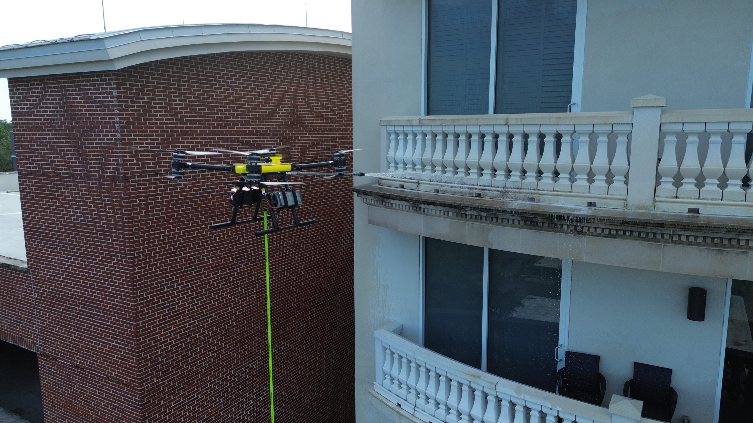 Drone soft washing a brick office building balcony and facade