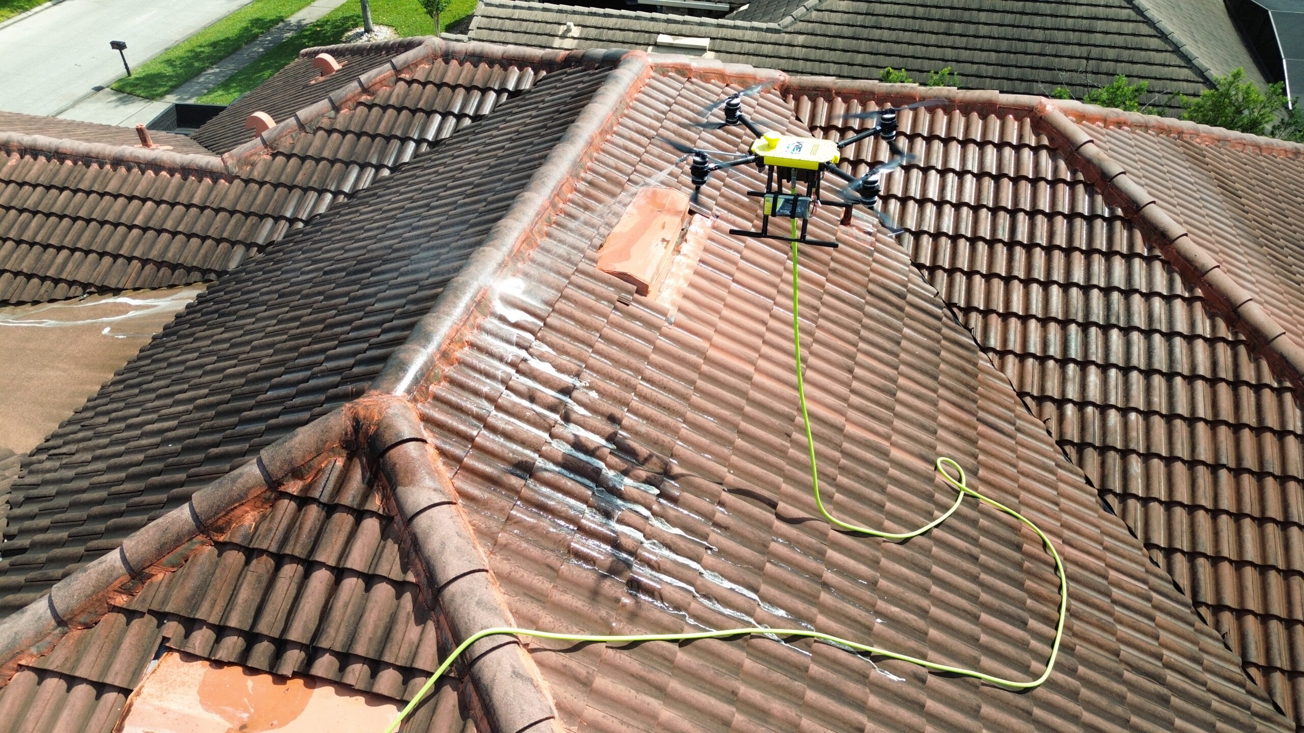 Tethered drone soft washing a tile roof, showing cleaned and uncleaned sections
